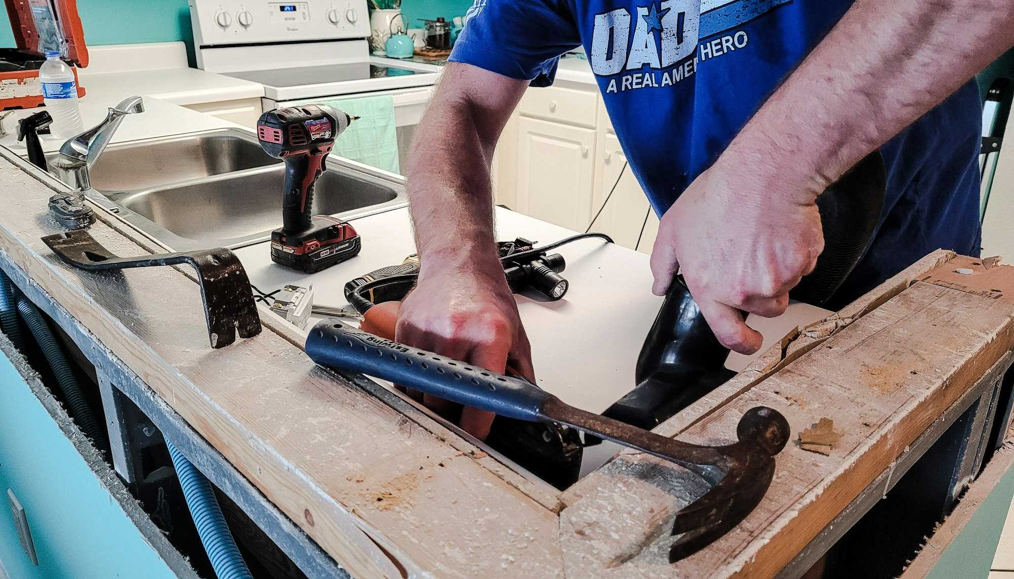 Demolition of Kitchen countertop in progress using several tools and hands.